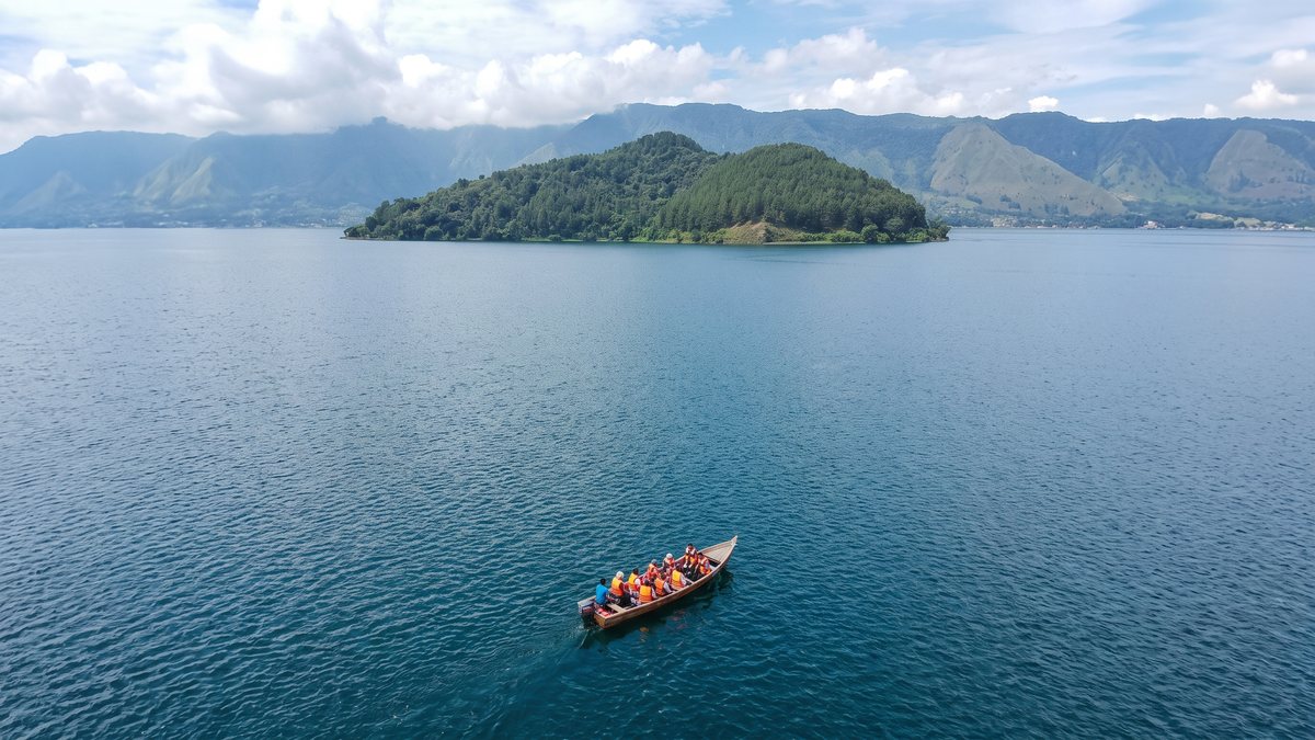 Perahu kecil di atas Danau Toba dengan pulau berhutan di kejauhan