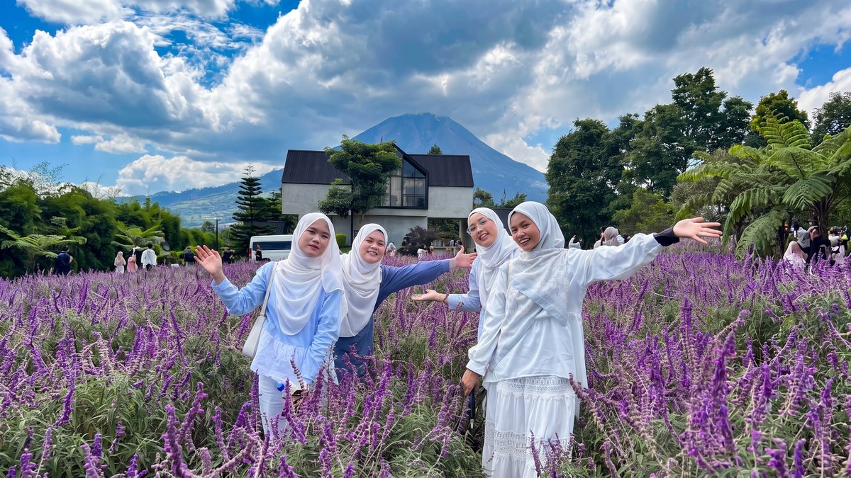 Peserta berfoto di kebun bunga dengan gunung dan rumah adat di belakangnya